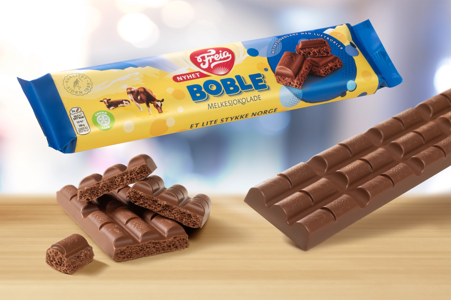 En sjokoladebar med boble- og melkekjeksdekor, plassert på et lyst bord, med noen bruttede sjokoladestykker foran.