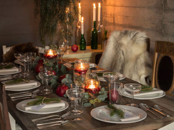 Et julebord med lyslenker, stearinlys, vinflasker og pyntede tallerkener på et bord, klar for festligheter.