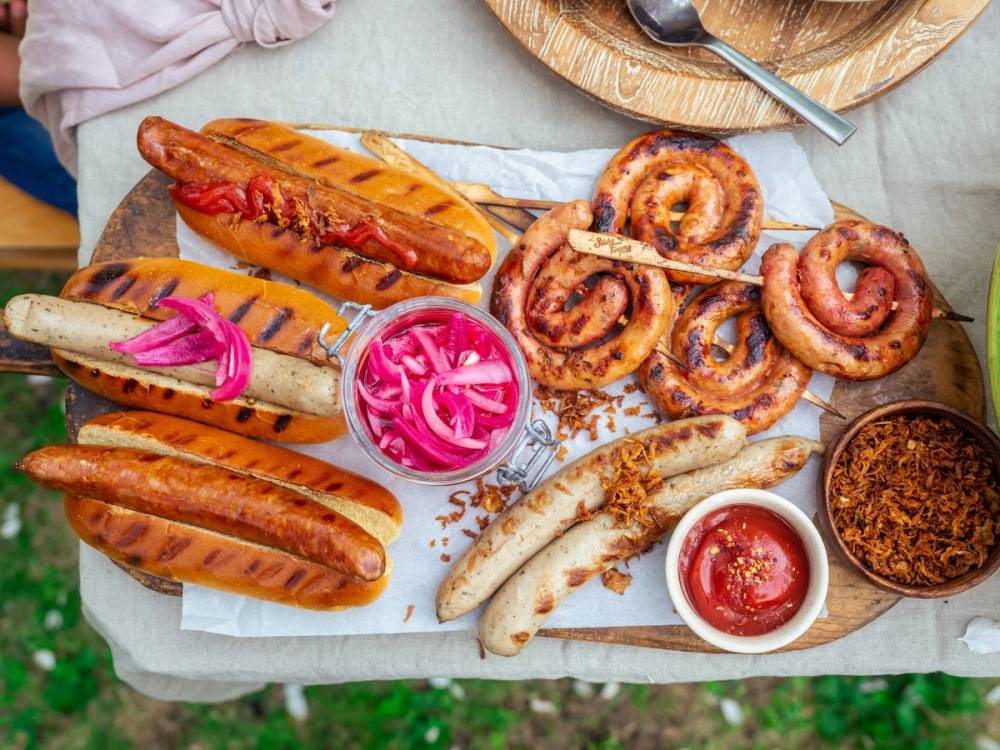 Et fat med ulike pølser, løkringer, en liten skål med surkål, ketchup og sennep, på et bord dekket med et hvitt stoff.