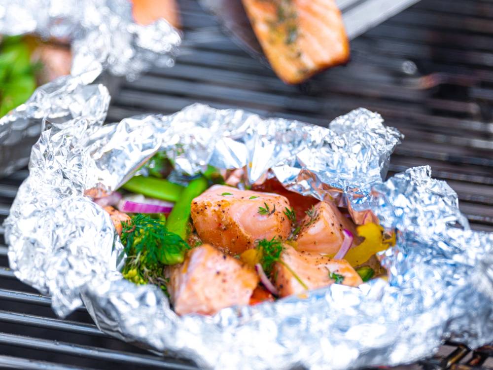 Grillet fisk og skalldyr pakket inn i aluminiumsfolie med grønnsaker rundt, på en grillplate