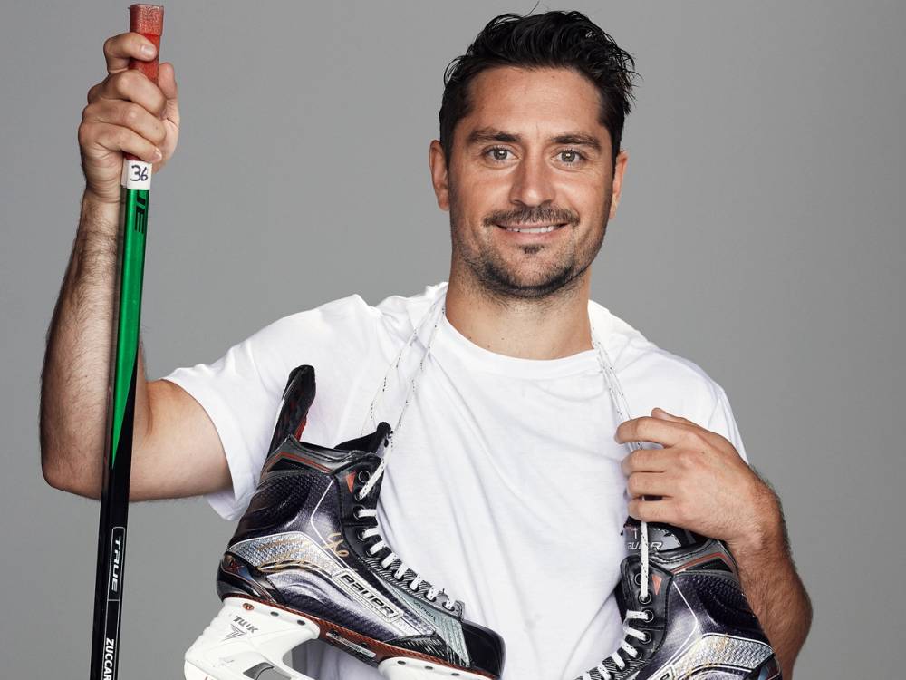 Person holder en ishockeykølle og har skøyter hengende over skulderen, med ansiktet utelatt for anonymitet.