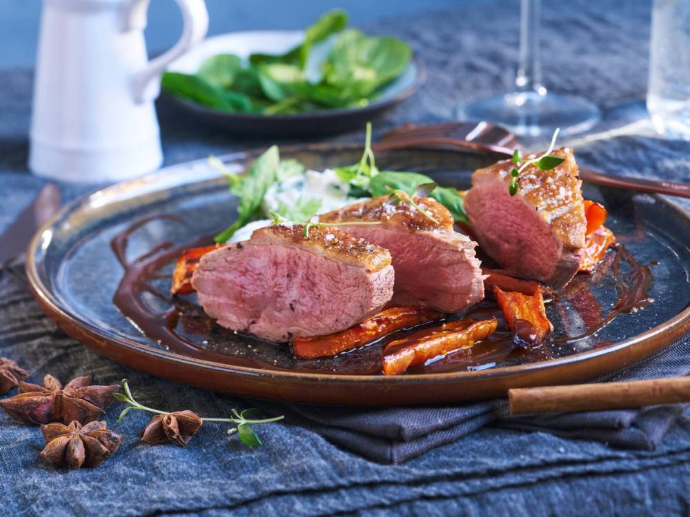 Andebryst skåret opp på en tallerken med grønnsaker og saus, ser ut til å være en ferdiglaget rett.