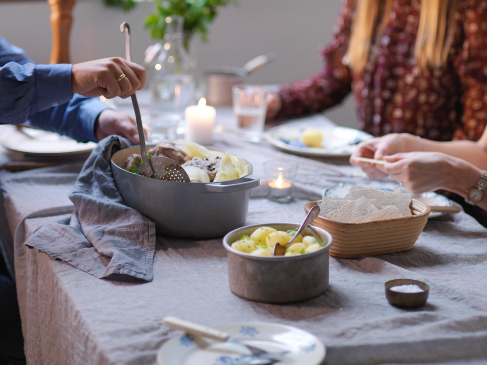 Fårikål serveres på et bord med flere personer som spiser og har samtale.