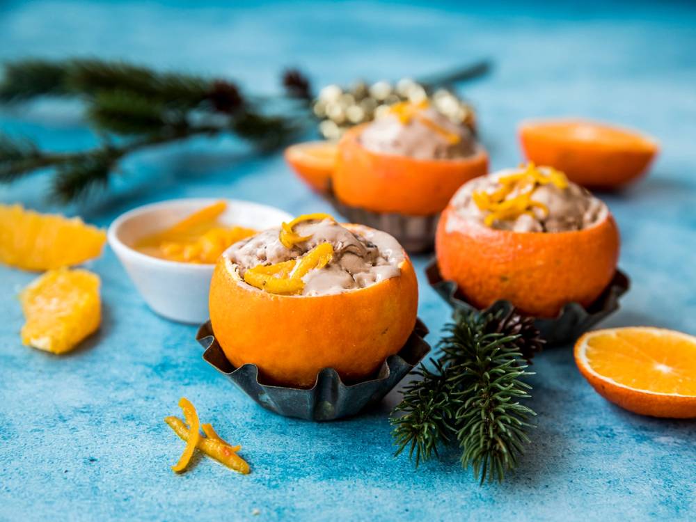 Klementiner fylt med sjokoladeis og pyntet med sitrusbåter og granbar på et blått bord.