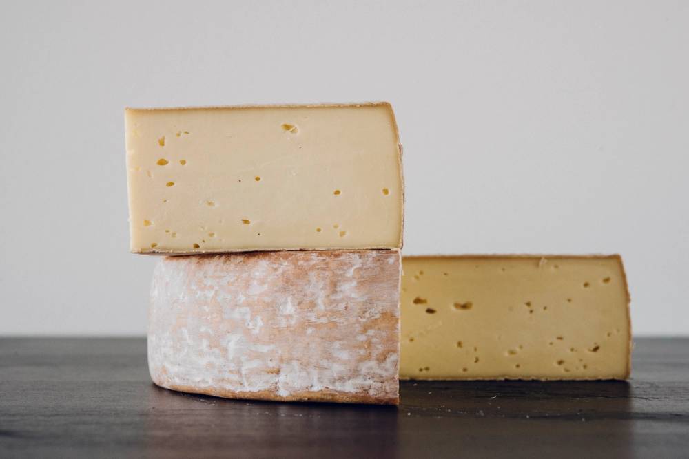 To ulike typer ost på en treplate, med en blokk av hard ost og en mindre ost med hvit skorpe, på et lyst bord.
