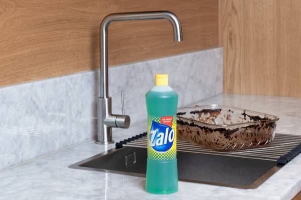 En kjøkkenvask med en grønn Zalo-flaske og en ildfast form med rester av mat på en benk