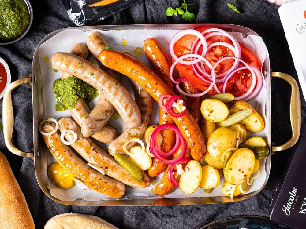 Ulike typer pølser, poteter, tomater og løk på et serveringsfat.