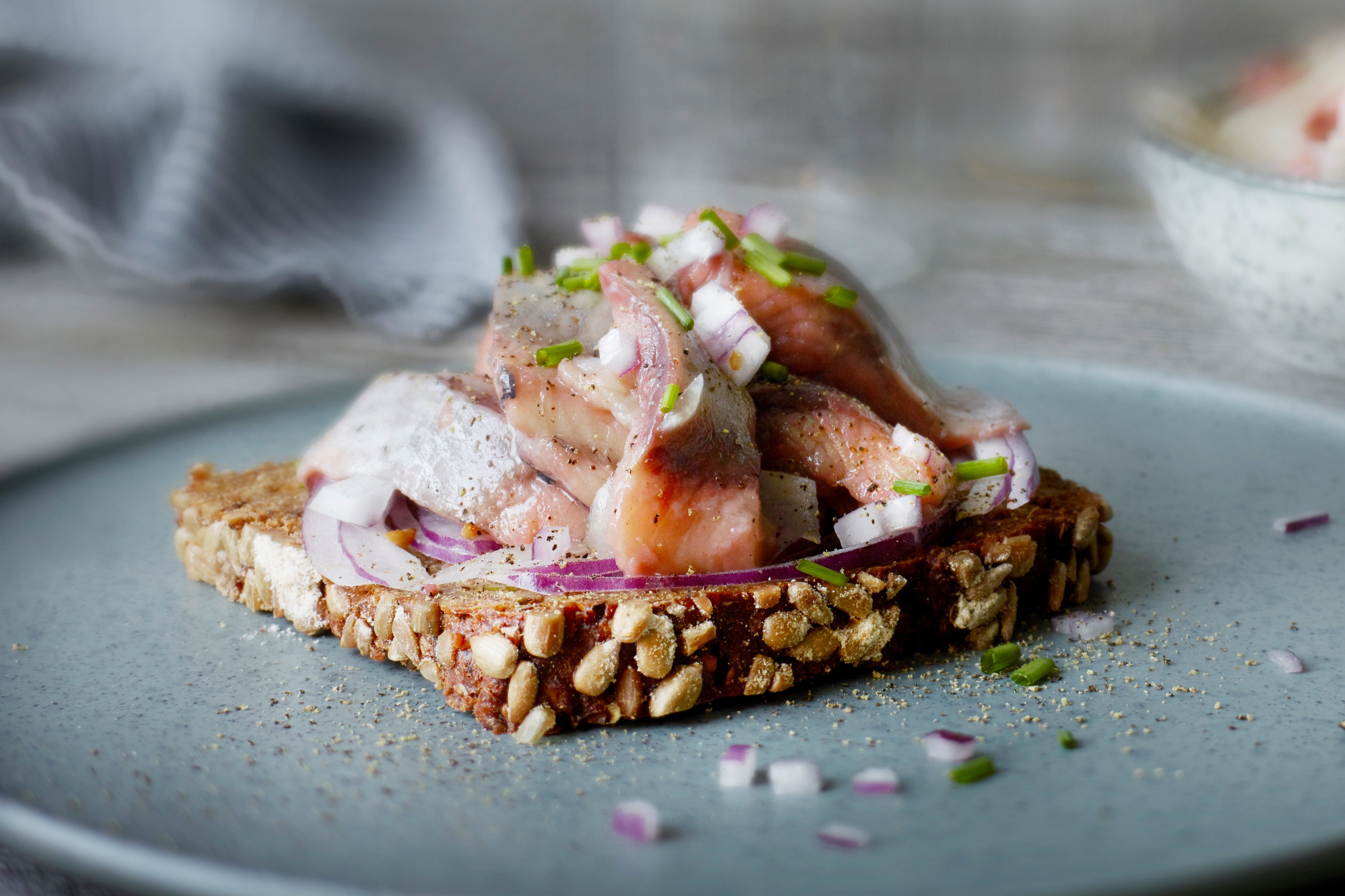 En skive med hjemmelaget pålegg med kylling, løk og grønne urter, ser ut til å være på en tallerken med nøtter og frø på, på et kjøkkenbord.