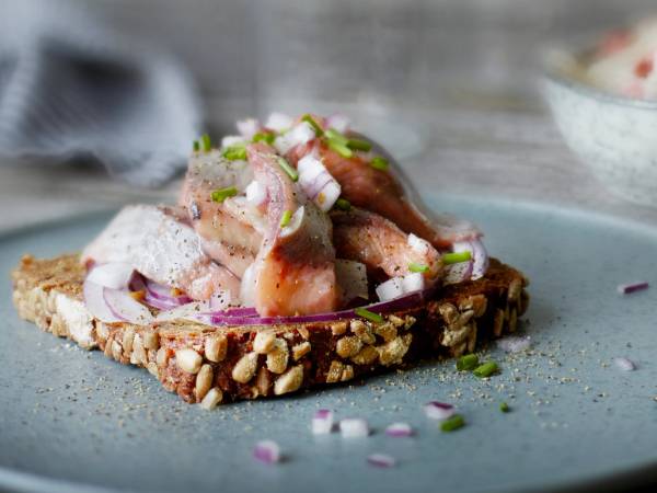 En skive med hjemmelaget pålegg med kylling, løk og grønne urter, ser ut til å være på en tallerken med nøtter og frø på, på et kjøkkenbord.