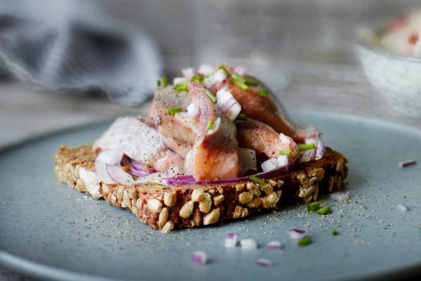 En skive med hjemmelaget pålegg med kylling, løk og grønne urter, ser ut til å være på en tallerken med nøtter og frø på, på et kjøkkenbord.