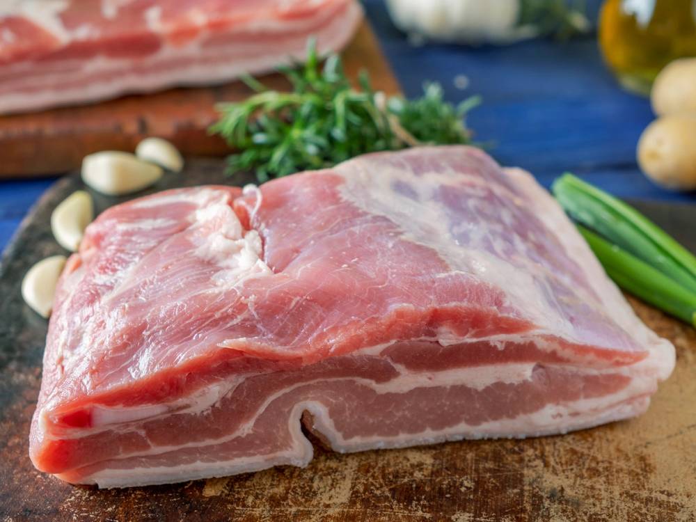 Siden av en buklist med lagvis fett og kjøtt, plassert på et skjærebrett med grønnsaker rundt.