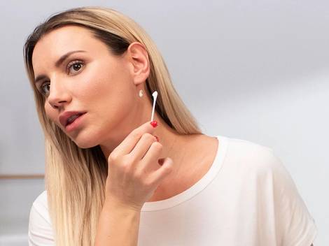 En person med langt blondt hår som bruker en bomullspinne til å påføre hårfarge hjemme, sett fra siden.