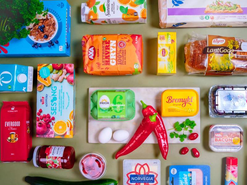 Et utvalg av matpakkeprodukter som juice, kjeks, ost, skinke, egg, og frukt, lagt ut på et bord.