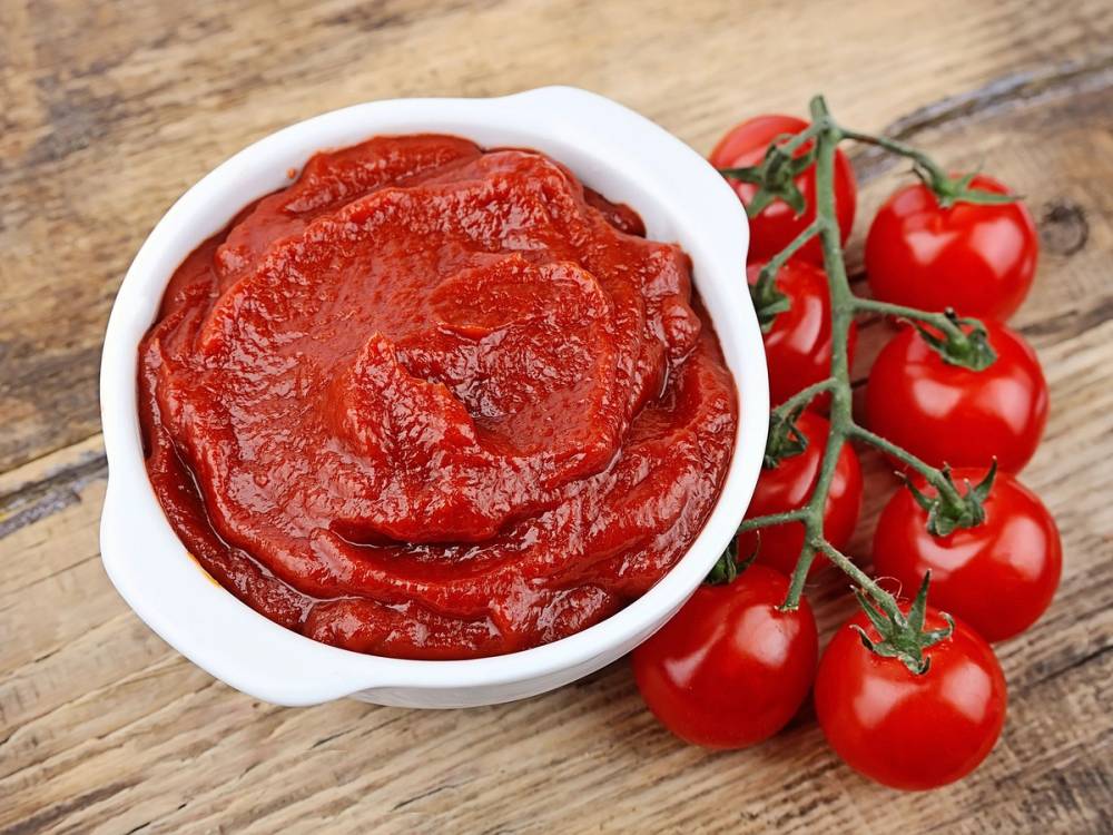Hjemmelaget ketchup i en hvit skål med cherrytomater på en treplate ved siden av
