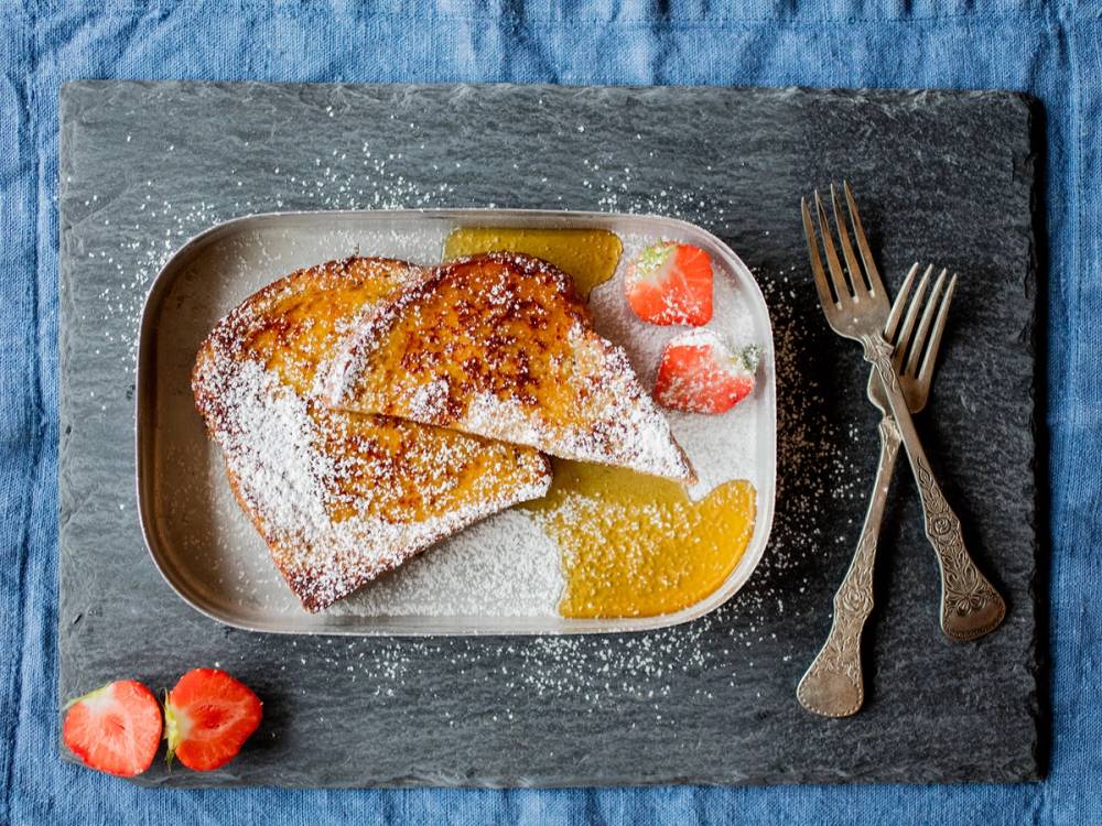 Arme-Riddere ser ut som sprøstekte brødskiver med sukker og frukt ved siden av på en tallerken.