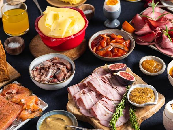 Et julefrokostbord med ulike retter, pålegg, egg, ost, og julepynt, sett på et mørkt bord.