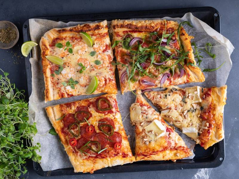 Fire typer pizza med ulike fyll, servert på et stekebrett med bakepapir.