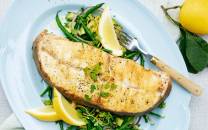 Grillet kveite med aspargesbønner og sitronbåter på en hvit tallerken, med en sitron og en grønn gren i bakgrunnen.