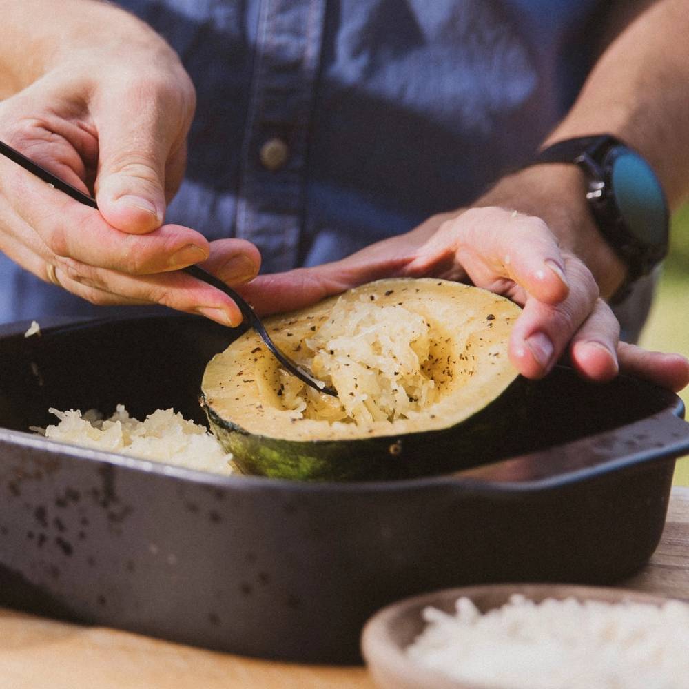 Person som bruker en gaffel til å skrape ut innholdet av et spagettigresskar, med en svart gryte foran og en liten skål ved siden av.