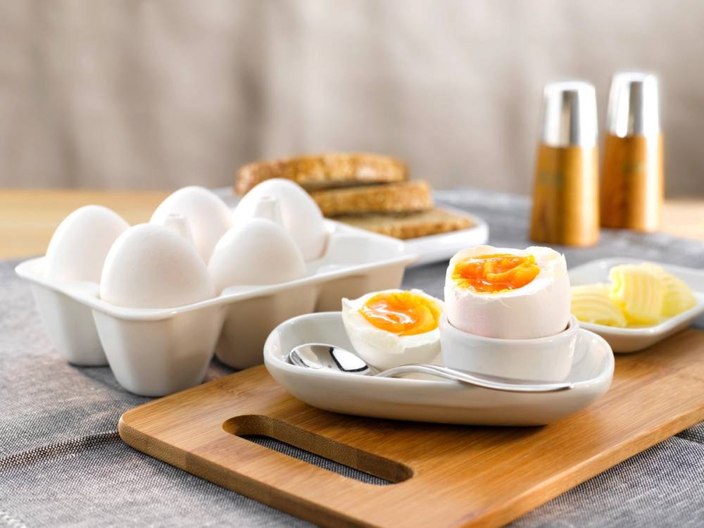 Kokt egg delt i to med en flytende plomme, servert på en hvit tallerken med smør og toast i bakgrunnen.