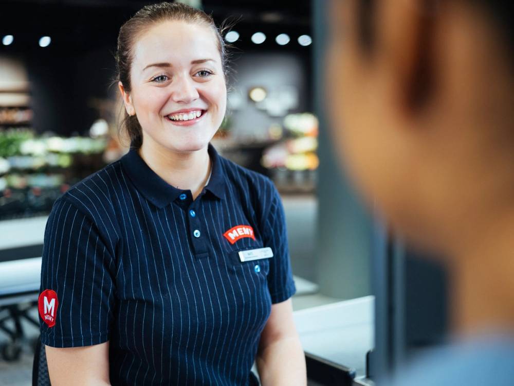 En ansatt i en butikk snakker med en kunde, med fokus på den ansatte som har på seg uniform og navnepinne.