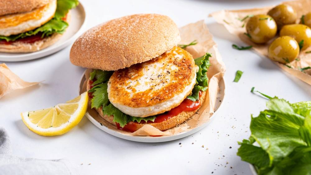 Fiskekaker i et hamburgerbrød med salat og tomat, servert med sitron og grønne oliven på siden.