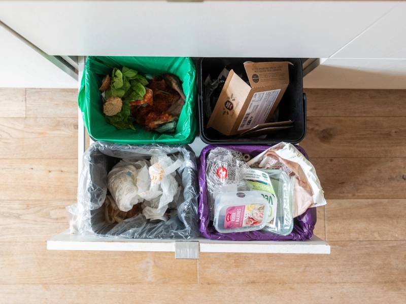 Åpnet kjøkkenskuff med fire oppbevaringsbokser fylt med matvarer og emballasje, plassert på en trebenkeplate.