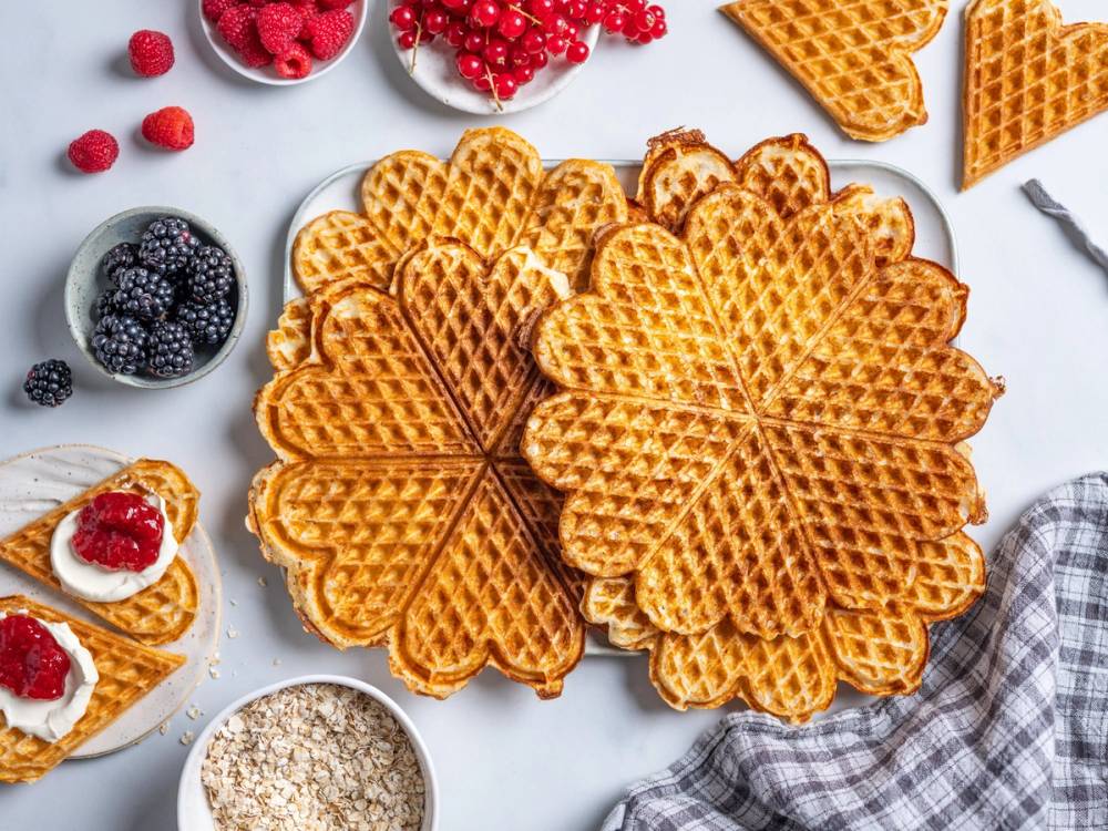 Grove vafler på et hvitt fat med bær og syltetøy rundt, klar til servering.