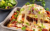 En tallerken med enchiladas fylt med kylling og dekket med ost og grønne erter, klar til å serveres.