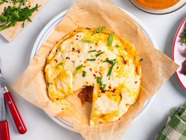 En liten pizza med ost, grønne urter og krydder på et hvitt fat med brunt bakepapir under, omgitt av andre retter og bestikk.