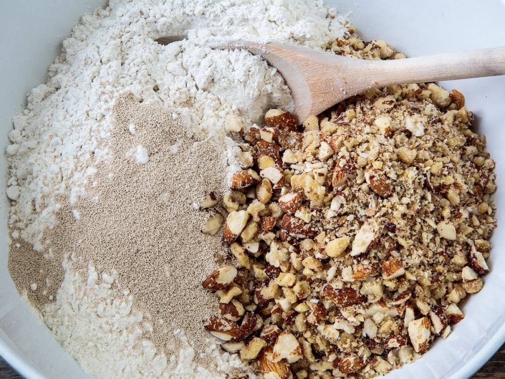 Blanding av grovbrøddeig med nøtter og mel i en bolle, klar for å bli eltet.