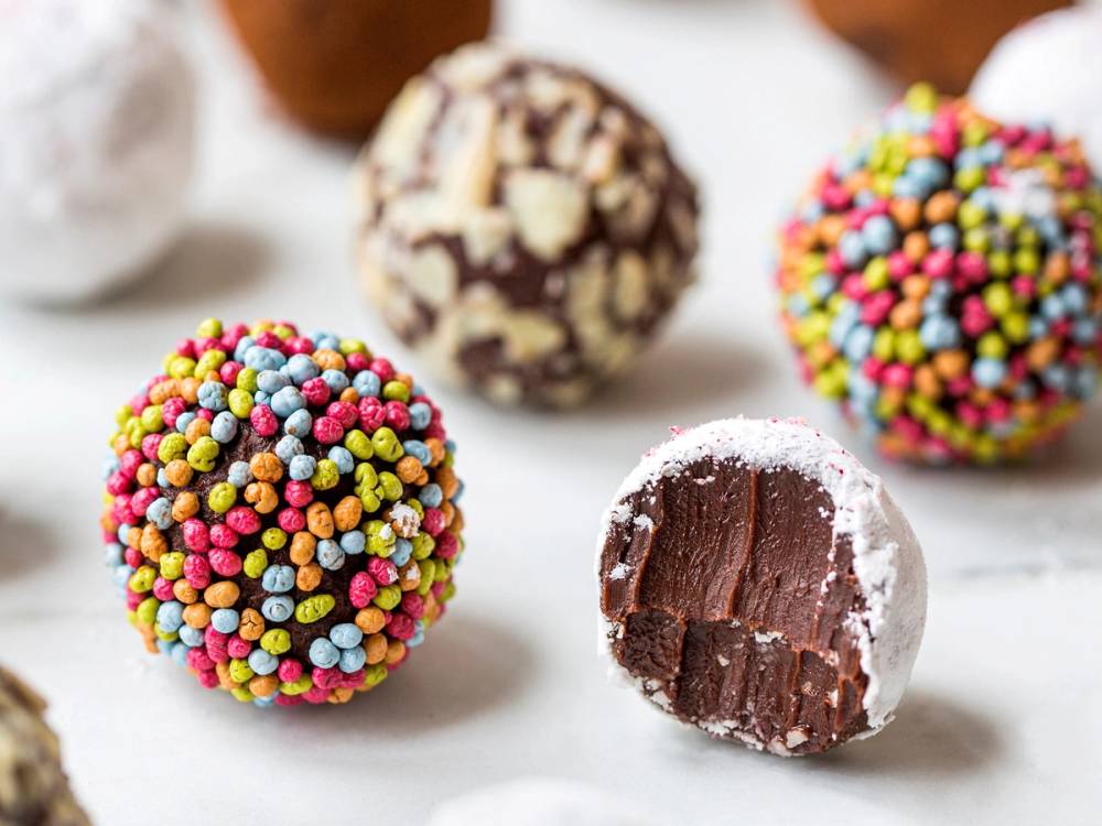 Fargede sjokoladetrøfler med sprøytede fargerike non-stop og en halvspist trøffel som viser sjokoladefyllet inni.
