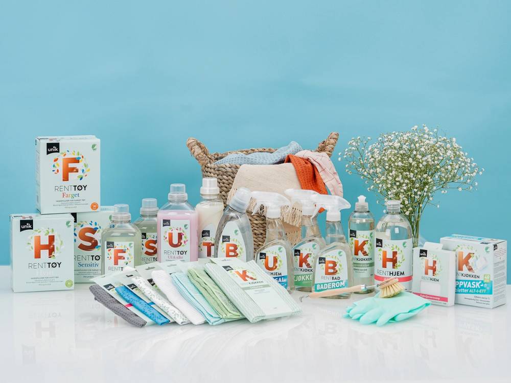 Et utvalg av blå rengjøringsprodukter og hygieneartikler på et bord, med blomster i bakgrunnen.