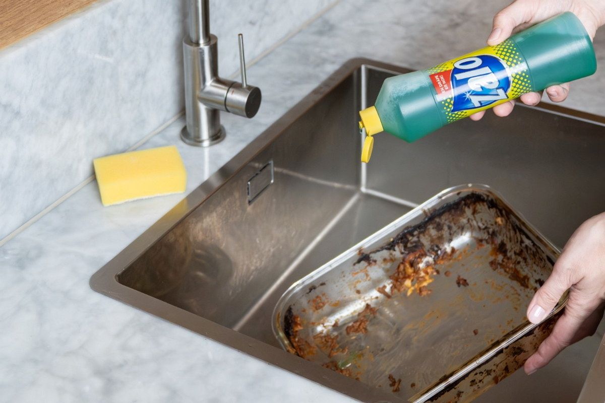 Person som bruker oppvaskmiddel for å rengjøre en stekeplate i kjøkkenvasken.