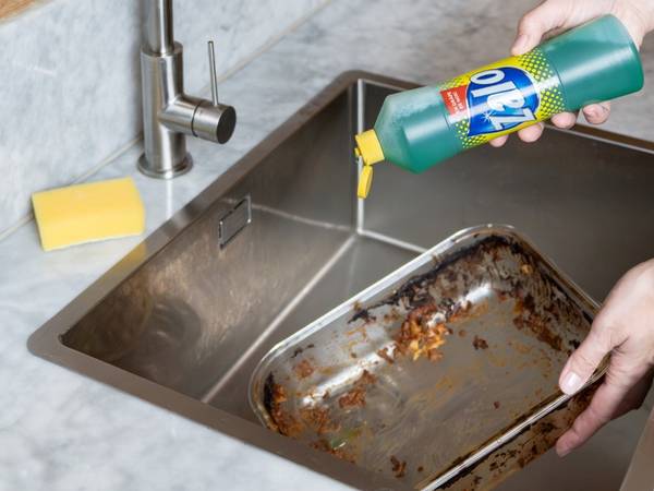 Person som bruker oppvaskmiddel for å rengjøre en stekeplate i kjøkkenvasken.