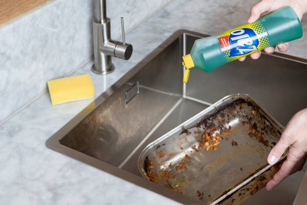 Person som bruker oppvaskmiddel for å rengjøre en stekeplate i kjøkkenvasken.