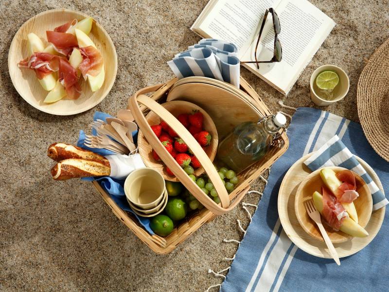 En piknik med mat og drikke på et utendørs underlag, inkludert frukt, ost, og en vannflaske, uten plastemballasje.