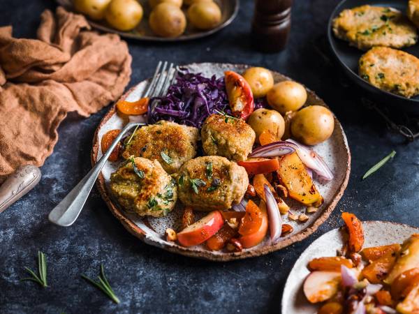 Vegisterkaker servert med kokte poteter og stekte grønnsaker på en tallerken, med en skje ved siden av.