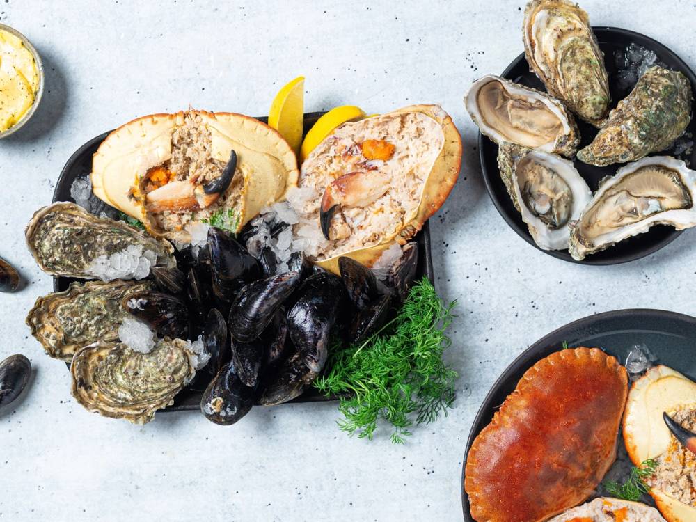 Skalldyr som østers og krabber på et fat med sitronbåter og grønn garnityr, klar for servering.