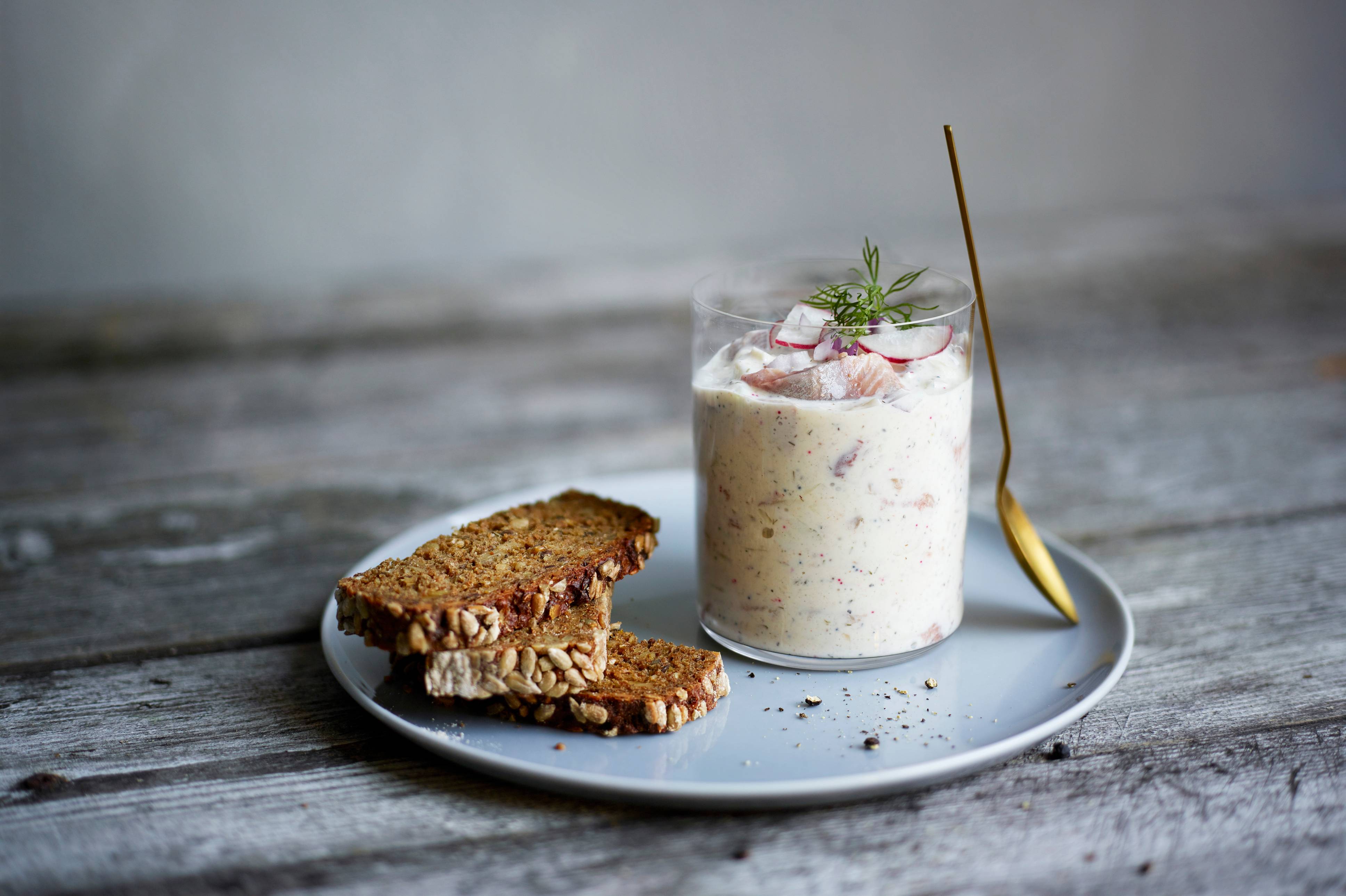 En glass med hjemmelaget yoghurt eller dessert med jordbær og mynte, sammen med to skiver grovt brød på en tallerken.