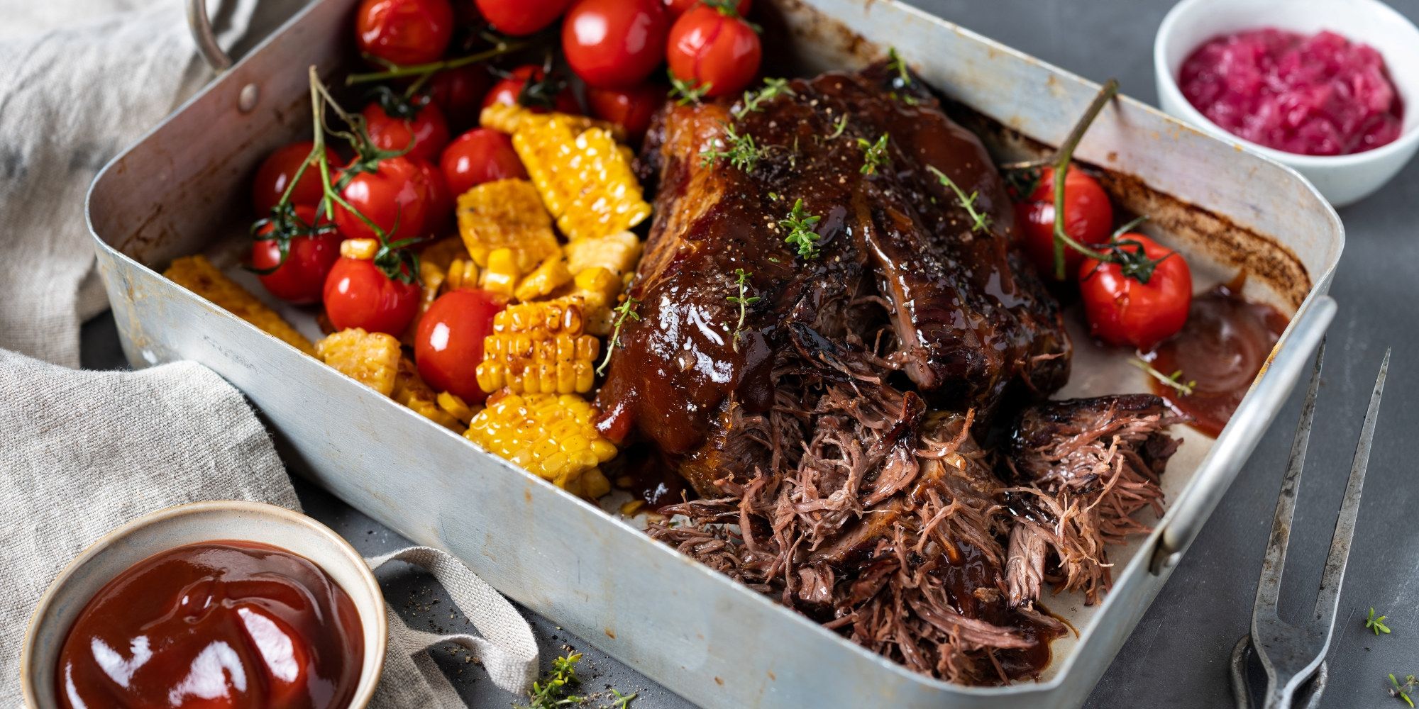 Pulled beef med cherrytomater, mais og en liten skål med rosa coleslaw på et fat.