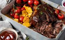 Pulled beef med cherrytomater, mais og en liten skål med rosa coleslaw på et fat.