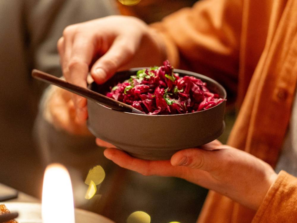 En person holder en svart bolle med rødkålsalat eller lignende, og bruker en skje til å servere den.