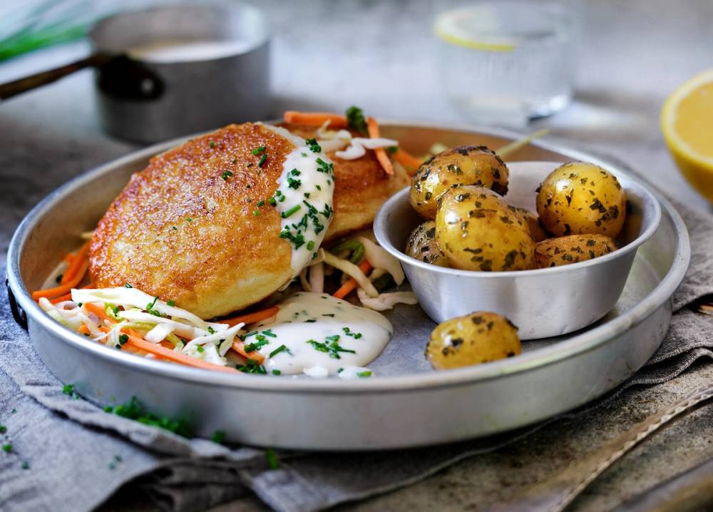 Fiskekaker servert med råkostsalat og små poteter på en tallerken.