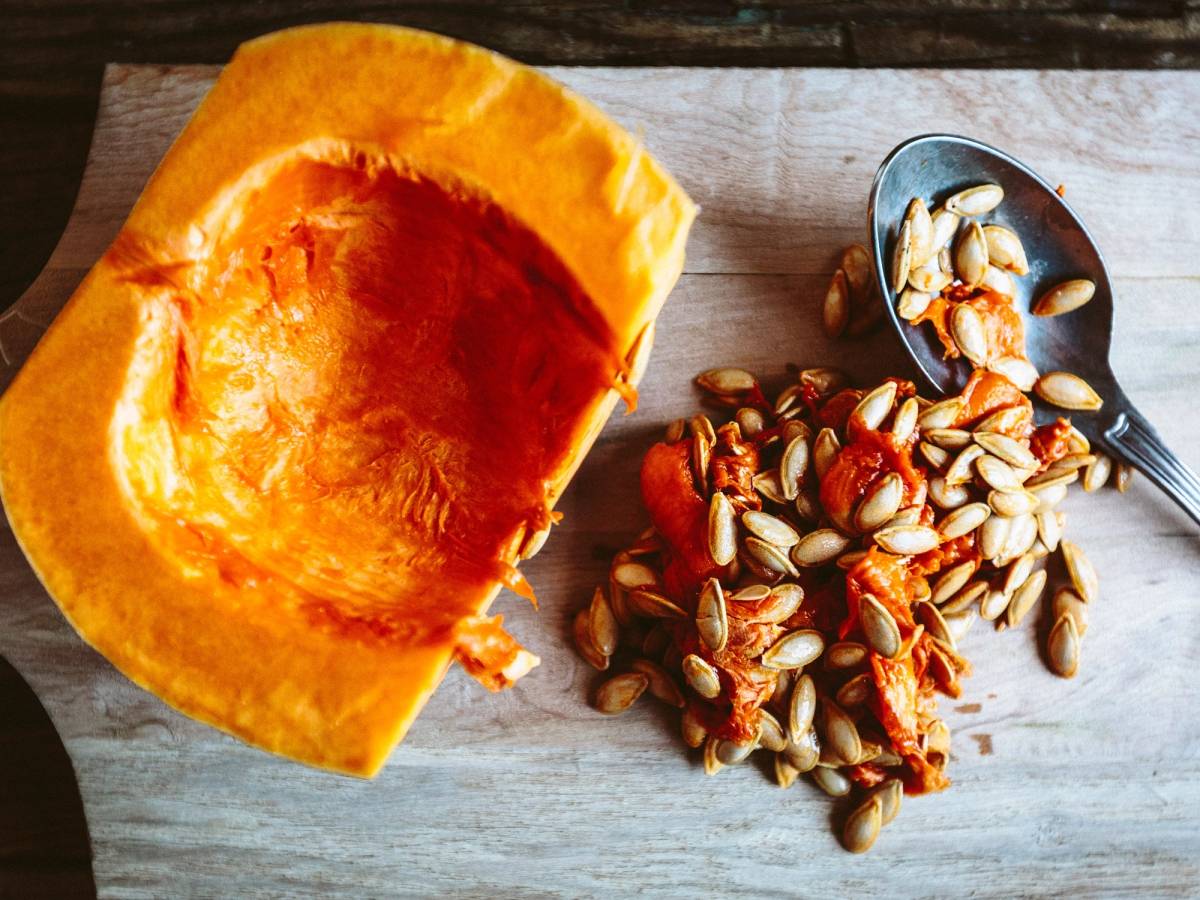 Ristede gresskarkjerner og en skje med noen av dem på et treplate, med en stor gresskarkjerne i fokus.