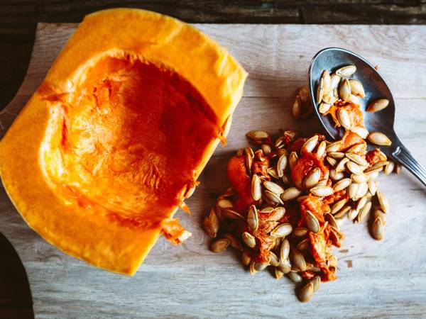 Ristede gresskarkjerner og en skje med noen av dem på et treplate, med en stor gresskarkjerne i fokus.