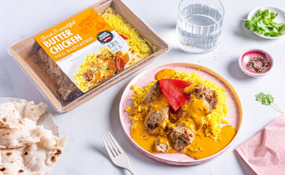 En tallerken med kylling i saus med ris, og en pakke med Takeaway Butter Chicken i bakgrunnen.