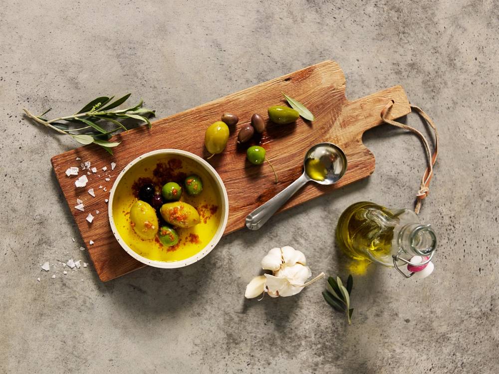 Marinerte grønne og svarte oliven på et trebrett med urter og olivenolje