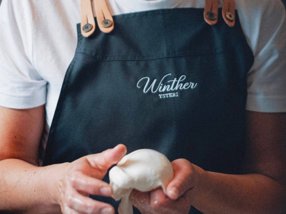 Person som holder en klump med ost i hendene, iført en svart Winther ysteri-forkle.