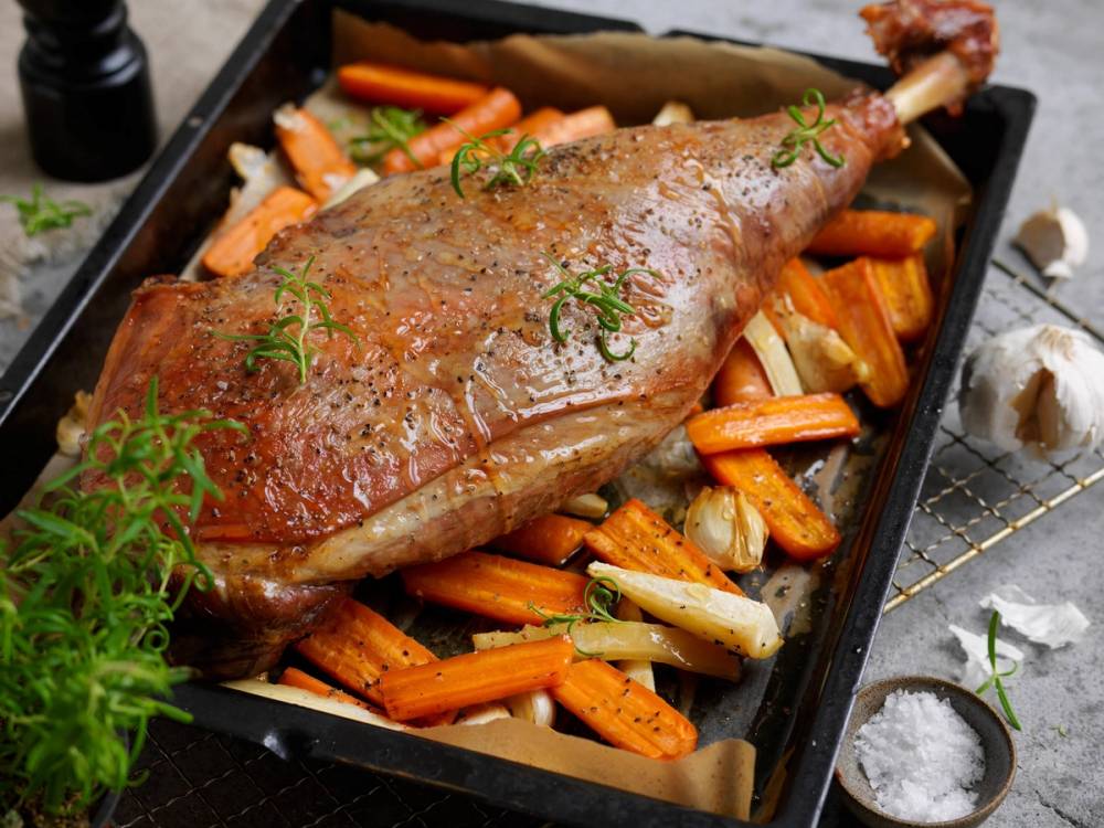 Stekt lammelår med ovnsstekte gulrøtter og selleristenger på en svart serveringsplate.